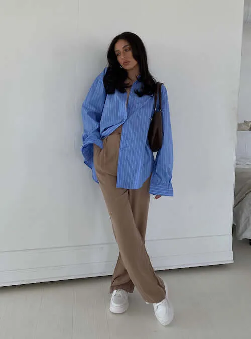 a woman wearing a blue button down shirt, tan linen pants, and white sneakers