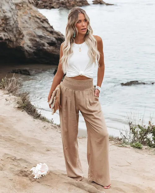 a woman wearing a white tank top and a pair of tan linen pants