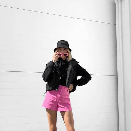 black jacket, pink shorts, and black hat