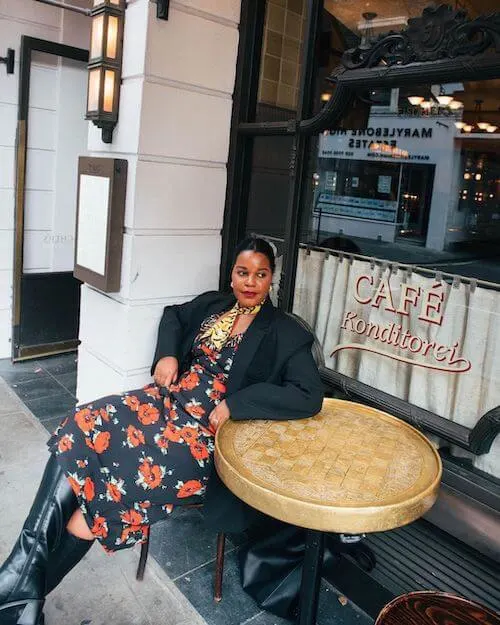 a beautiful black woman wearing a black coat and a long floral dress