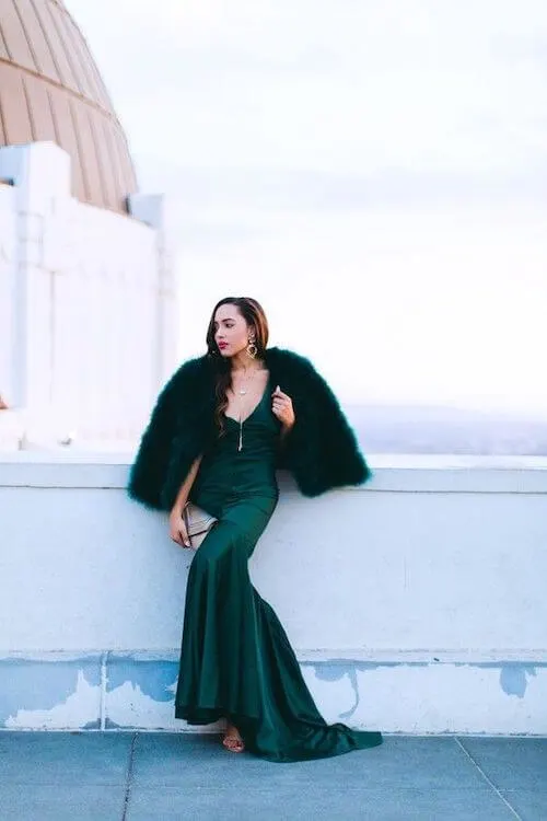 a woman attending a winter wedding wearing a dark green fur coat and a dark green formal dress