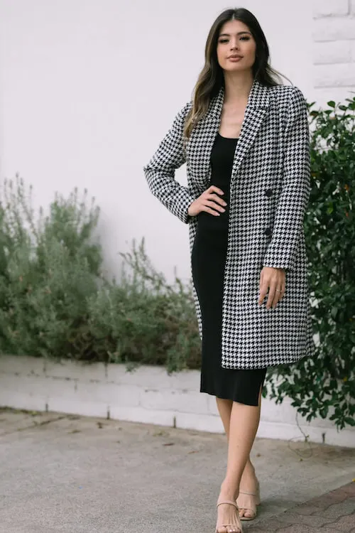 a woman wearing a long black dress and a long white black plaid coat