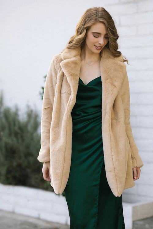 a woman wearing a camel faux fur coat and a green cami dress
