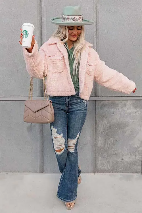 a woman wearing blush teddy coat, green button down shirt, light pink hat, and flare jeans
