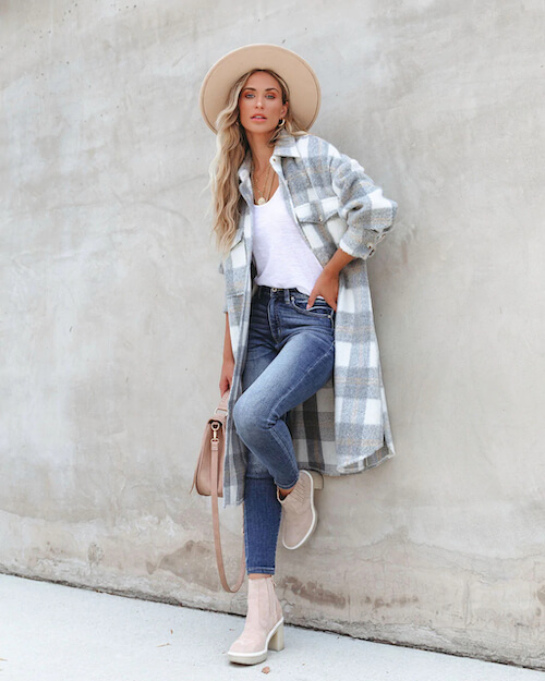 a woman wearing a long plaid coat, a white shirt, and a pair of blue jeans in winter