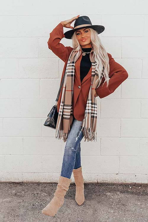 a woman wearing brown oversized blazer, scarf, skinny jeans, hat, and tan sock boots