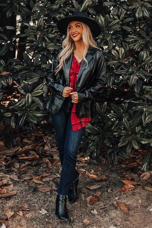 a woman wearing a black leather jacket, red plaid shirt, a pair of dark blue jeans, a pair of black ankle boots, and a black hat