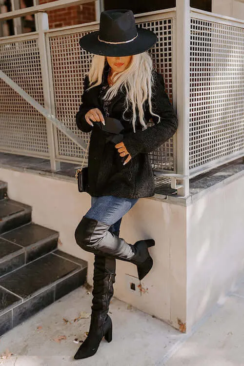 a woman wearing short black coat, blue skinny jeans, a pair of black thigh high boots, and a black hat