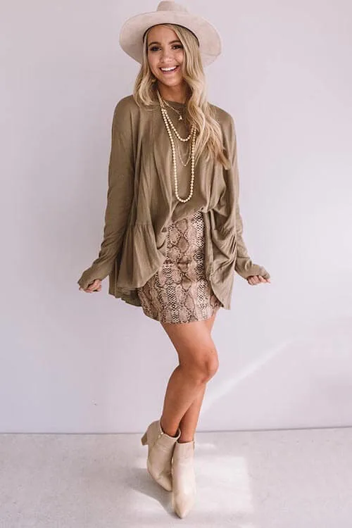 a woman in the party wearing olive green top, snakeskin leather skirt, tan boots, western hat, and western inspired necklaces