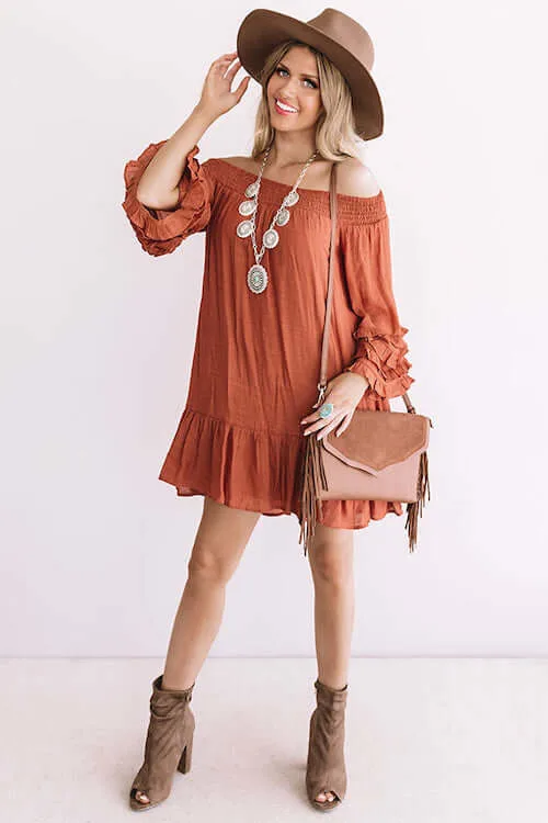 a woman wearing a western chic dress, western chunky necklace, brown boots, brown bag, and brown hat