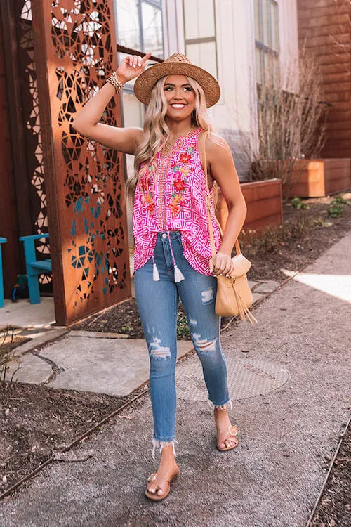 a woman wearing Nashville city in spring summer wearing a cute pink top, a pair of skinny jeans, sandals, and straw cowgirl hat